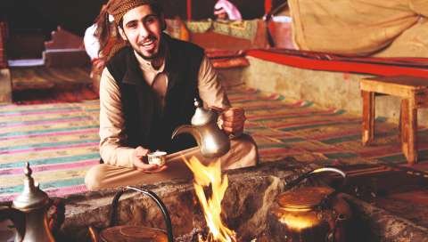 Arab man sitting on a carpet making traditional tea on a bonfire